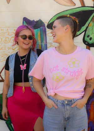 Two people standing in front of a colorful mural, one wearing a pink 'not straight' shirt.
