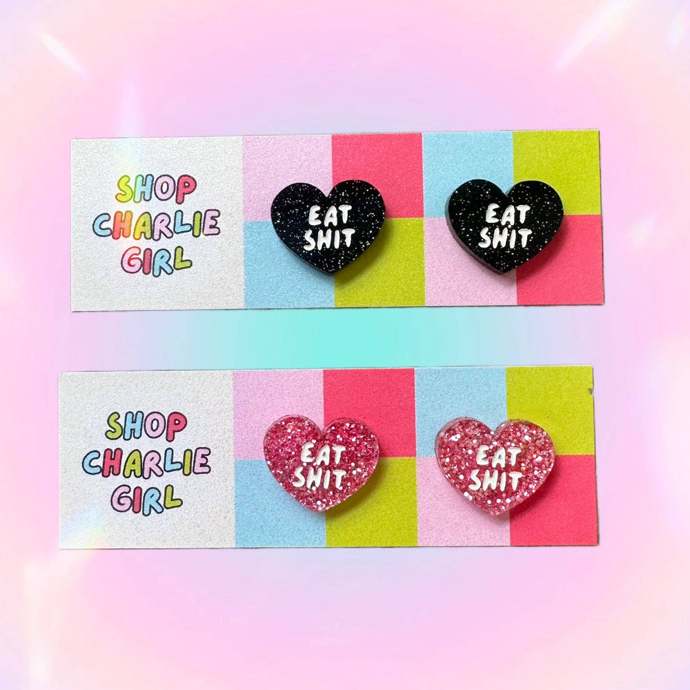 Heart-shaped earrings with 'EAT SHIT' text on a colorful card with 'Shop Charlie Girl' branding.