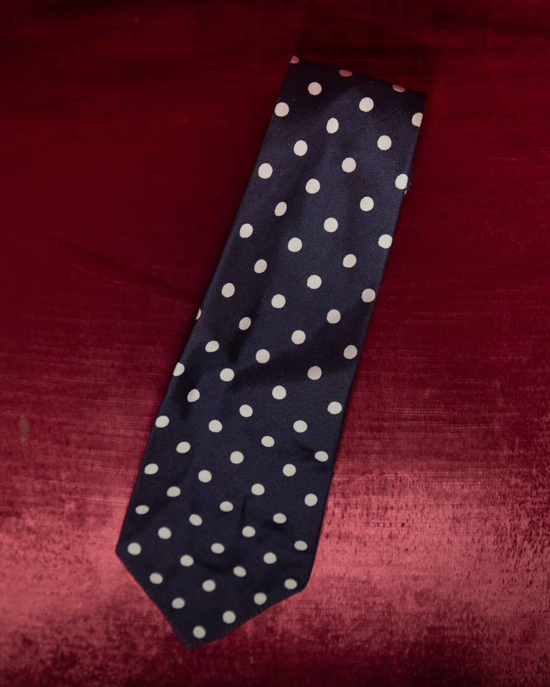 Navy blue tie with white polka dots on a red textured background
