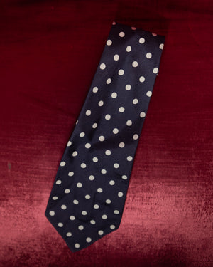Navy blue tie with white polka dots on a red textured background