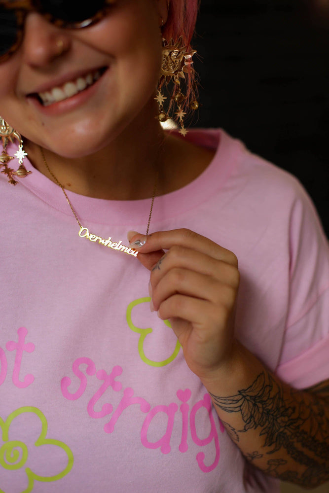 Person wearing a pink shirt with text and graphics, holding a gold necklace.