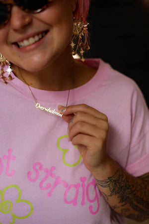 Person wearing a pink shirt with text and graphics, holding a gold necklace.
