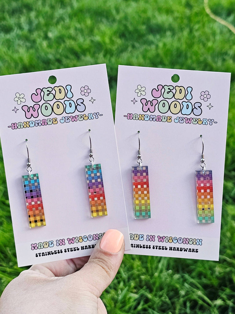 Colorful earrings on 'Jedi Woods' branded cards held against a grass background