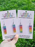 Colorful earrings on 'Jedi Woods' branded cards held against a grass background