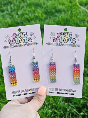 Colorful earrings on 'Jedi Woods' branded cards held against a grass background