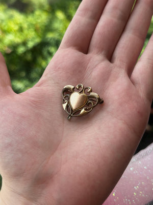 Gold heart-shaped pendant held in a hand with a blurred green background