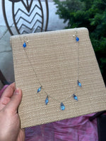 Jewelry display card with blue teardrop earrings held by a hand.