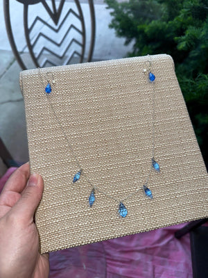 Jewelry display card with blue teardrop earrings held by a hand.