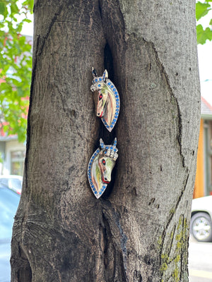 Two colorful horse-shaped objects attached to a tree trunk.